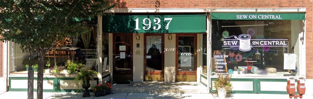 Exterior view of Sew on Central quilt shop, featuring a green awning with the shop's name prominently displayed, along with decorative elements and entrance.