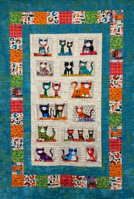 A quilt featuring a colorful cat pattern with playful cat illustrations framed by vibrant borders in various prints.