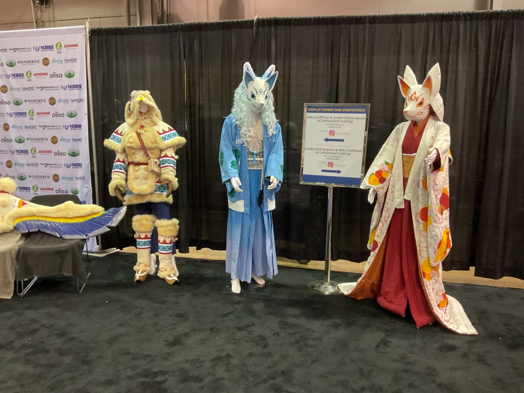 Cosplay display featuring three elaborate costumes at the H&H Americas Show, showcasing a blend of cultural elements and craftsmanship.