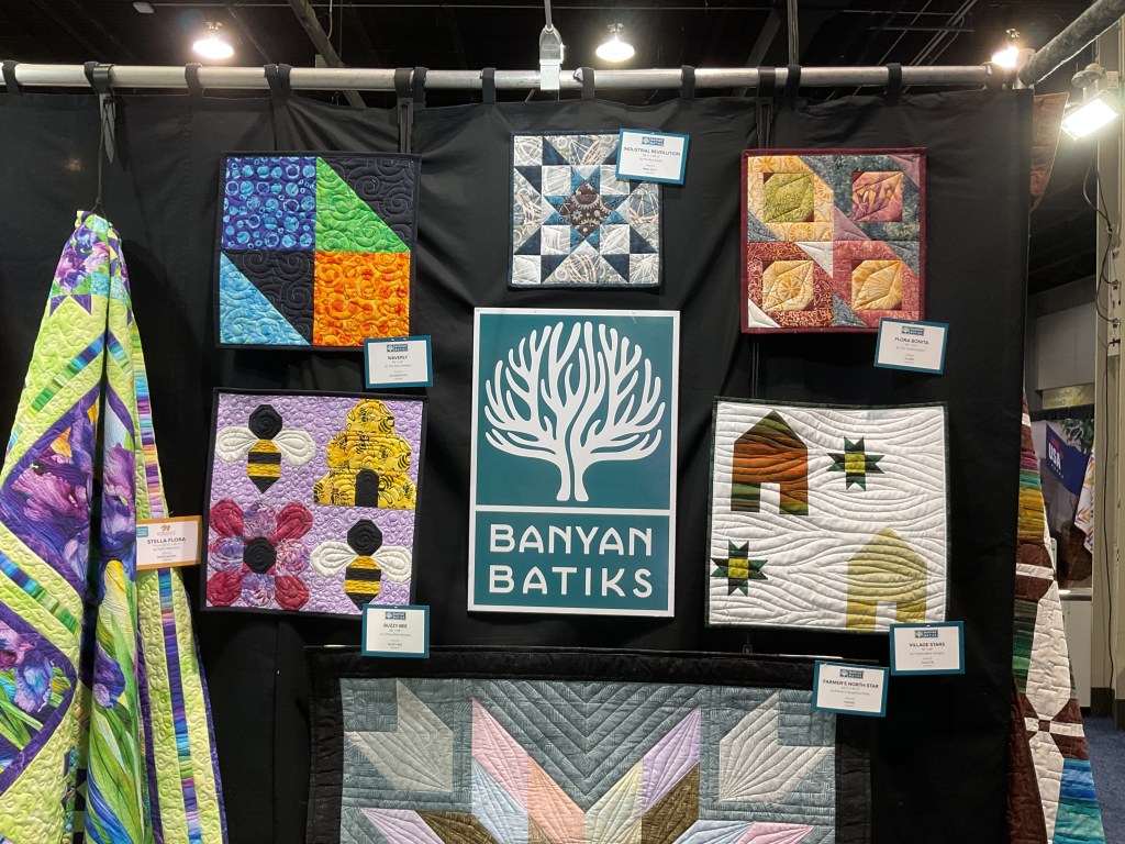 Display of various quilt blocks featuring colorful designs and patterns at the Banyan Batiks booth.