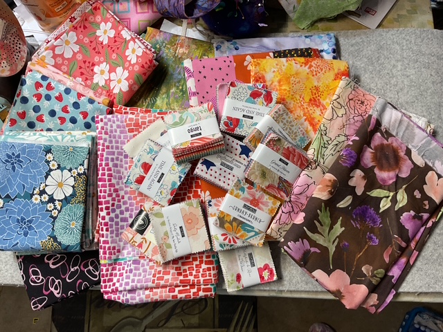 A collection of colorful fabric squares and charm packs arranged on a surface, showcasing various floral and geometric patterns.