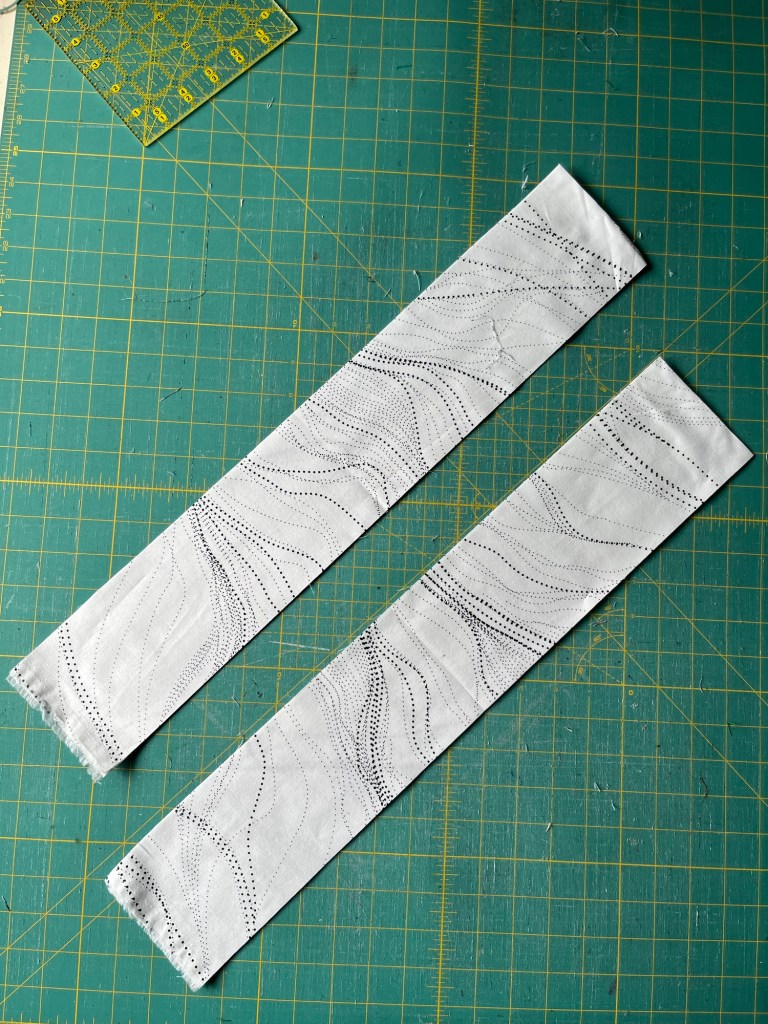 Two strips of fabric with a squiggly pattern on a cutting mat, showcasing a quilting project.