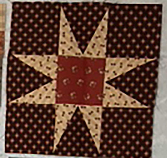 Patchwork quilt block featuring a star design in shades of brown and beige, with a red center.