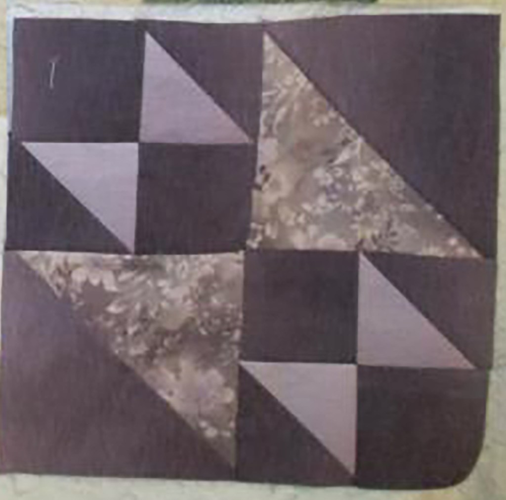 Quilt block featuring various triangular and square shapes in a muted color palette, showcasing different fabric textures.