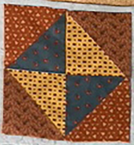 A quilt block featuring a geometric pattern with brown, gray, and yellow fabrics arranged in a pinwheel design.