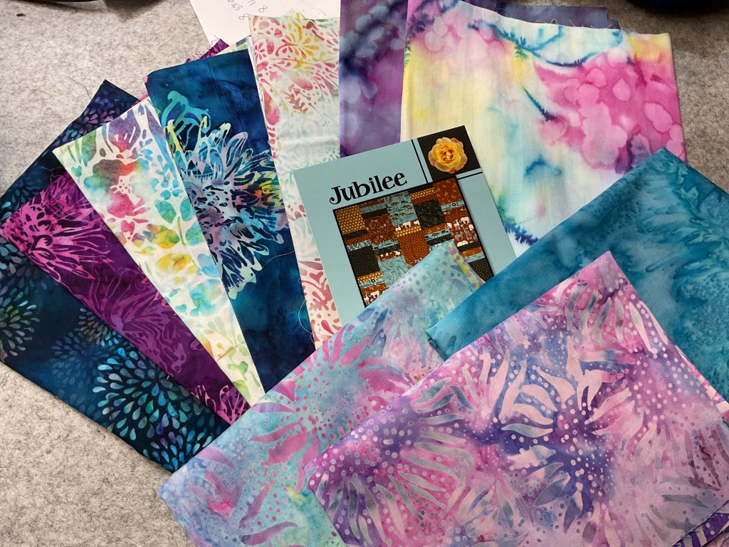 A collection of colorful batik fabrics arranged around a Jubilee quilt pattern, showcasing vibrant colors and intricate designs.