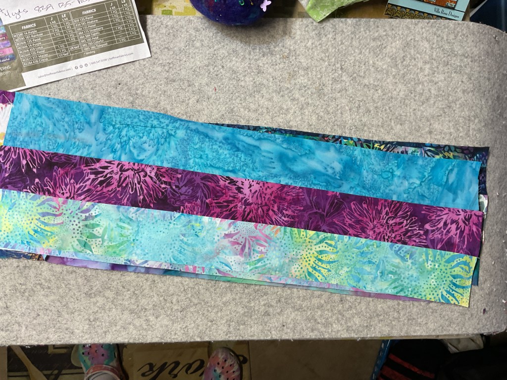 A collection of colorful batik fabric strips arranged on a cutting surface, ready for quilting.