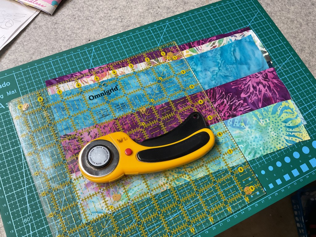 Cutting fabric squares with a rotary cutter and ruler on a cutting mat.