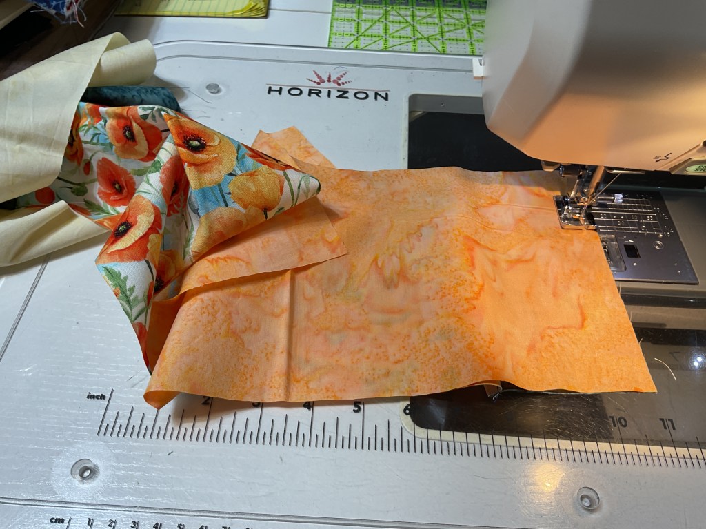A sewing machine with colorful fabric pieces, including floral and orange prints, laid out for stitching.
