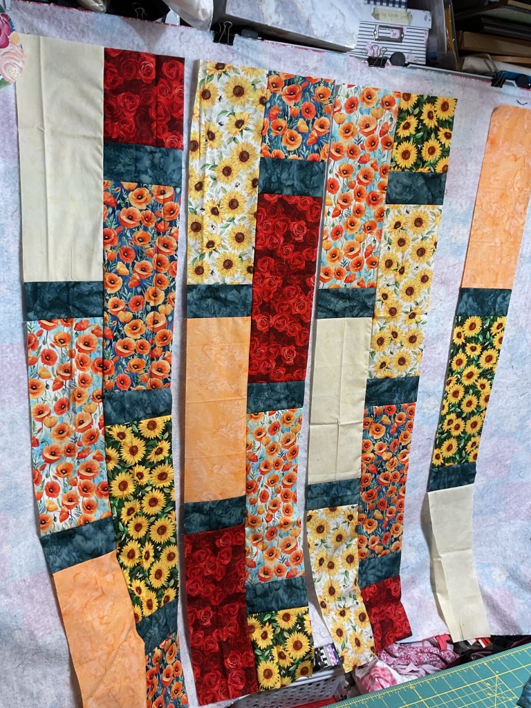 Vertical strips of colorful floral fabrics arranged on a flannel board in preparation for quilting.