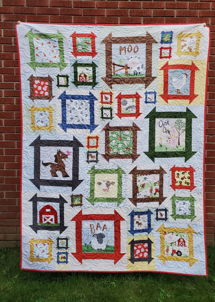 A colorful quilt featuring various farm animal-themed blocks framed with bold borders in different colors, displayed against a brick wall.