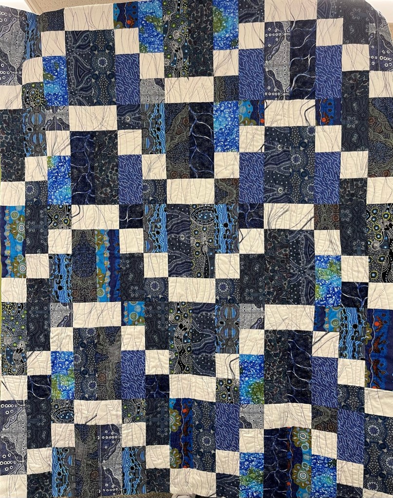 A quilt featuring a patchwork design with various shades of blue, turquoise, and white, arranged in a square pattern.
