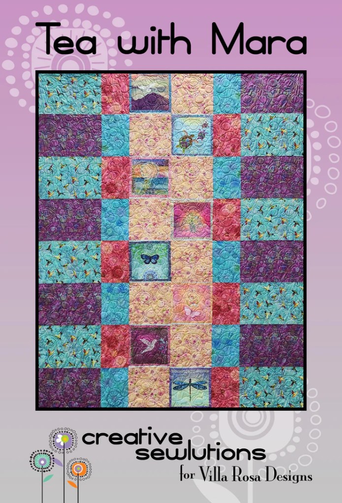 A colorful quilt titled 'Tea with Mara' featuring a patchwork design with floral and butterfly patterns, highlighting various shades of pink, blue, and purple.