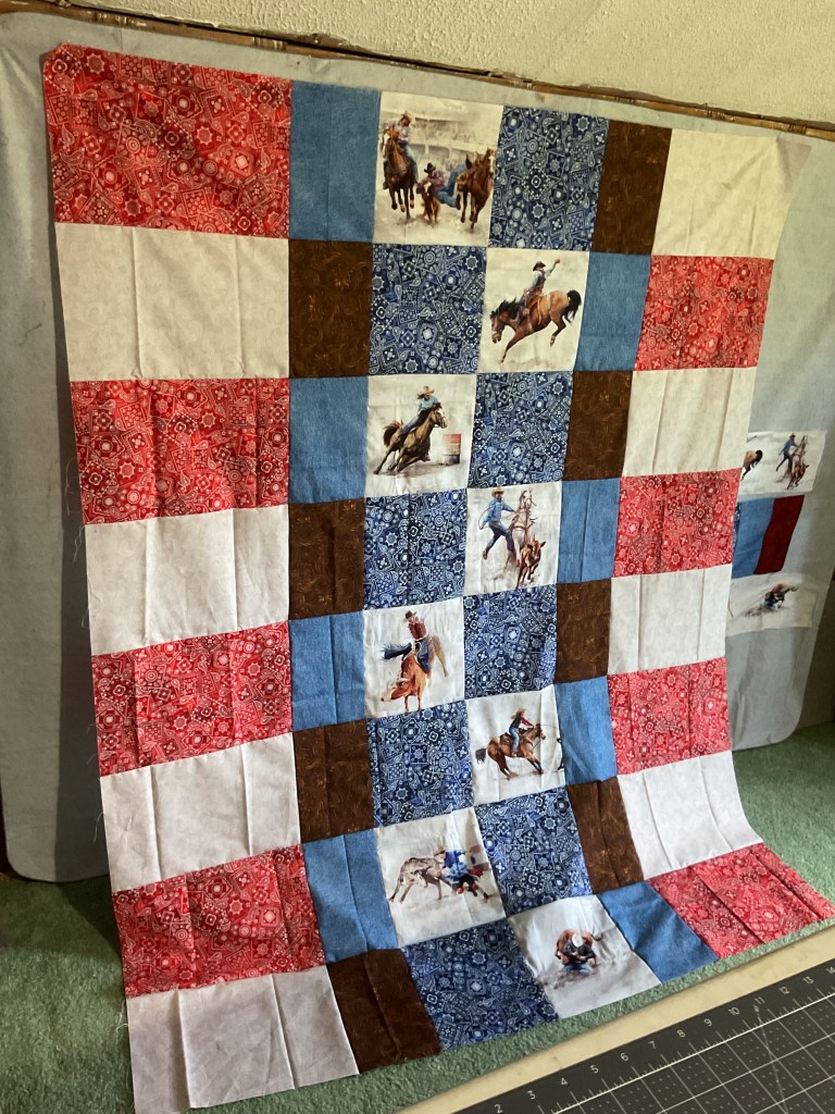A quilt with alternating squares of red, white, blue, and brown fabric, featuring images of rodeo scenes.
