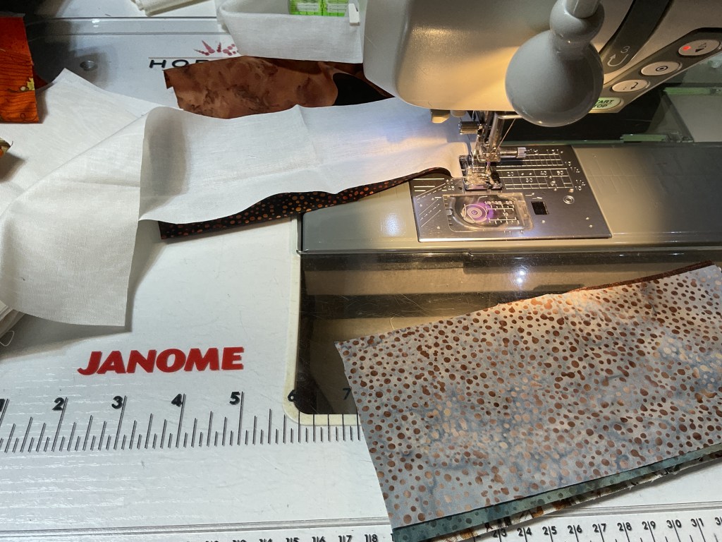 Close-up of a Janome sewing machine with fabric pieces and threading on the sewing table.