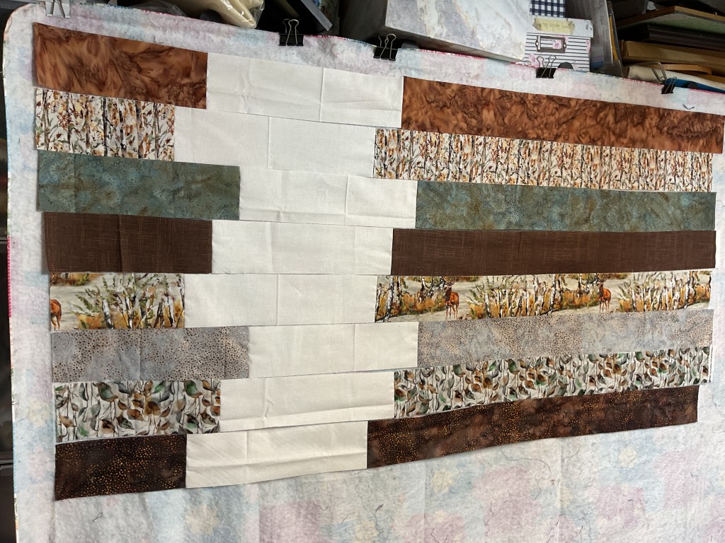 A patchwork quilt arranged with various fabric strips in earthy tones and patterns, displayed on a flannel board.