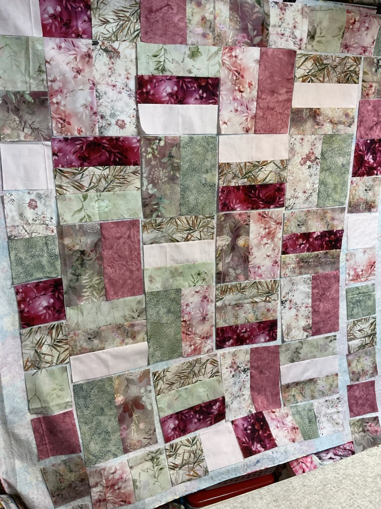 A colorful quilt top made of various fabric pieces in shades of pink, green, and white, arranged in a patchwork design.
