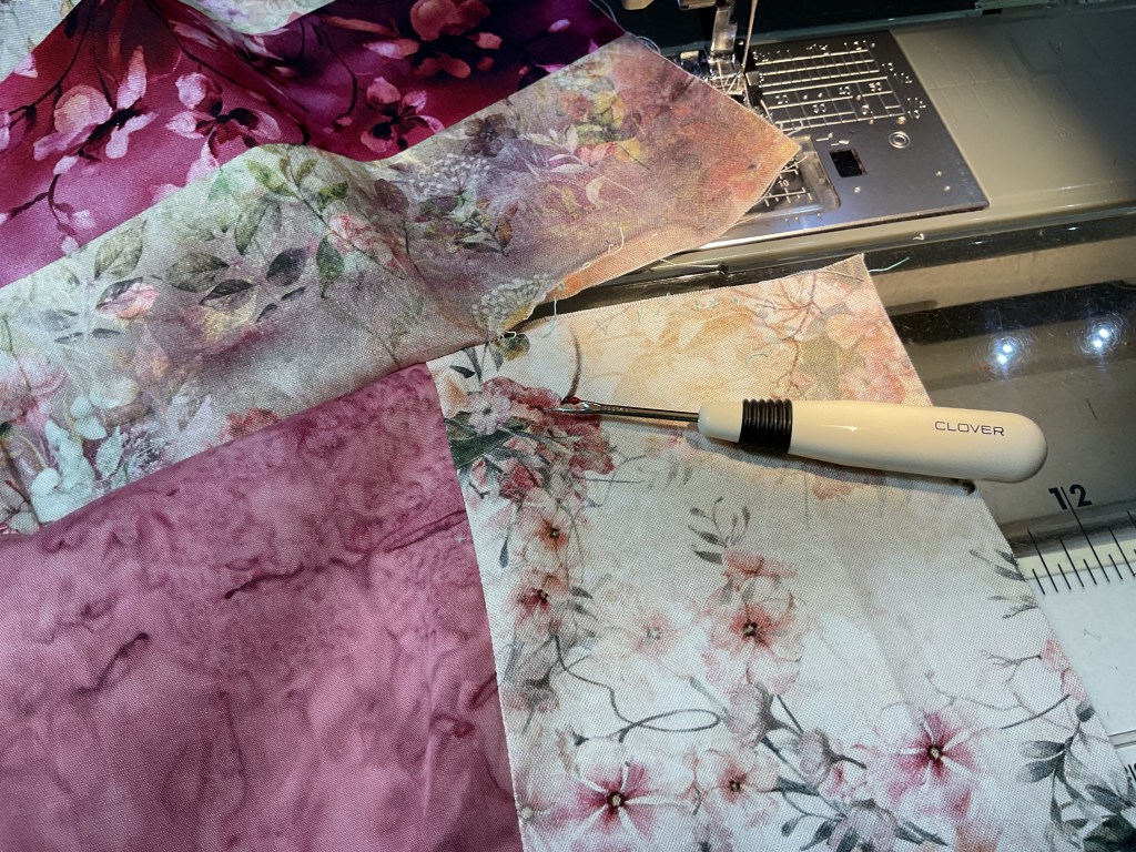 A sewing machine with floral fabric pieces positioned next to a seam ripper tool on a workspace.