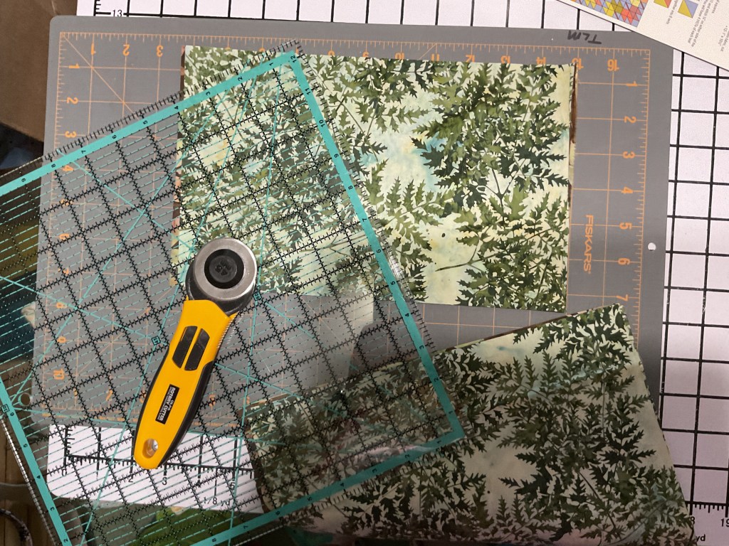 Cutting quilting fabric pieces on a cutting mat with a rotary cutter and ruler.