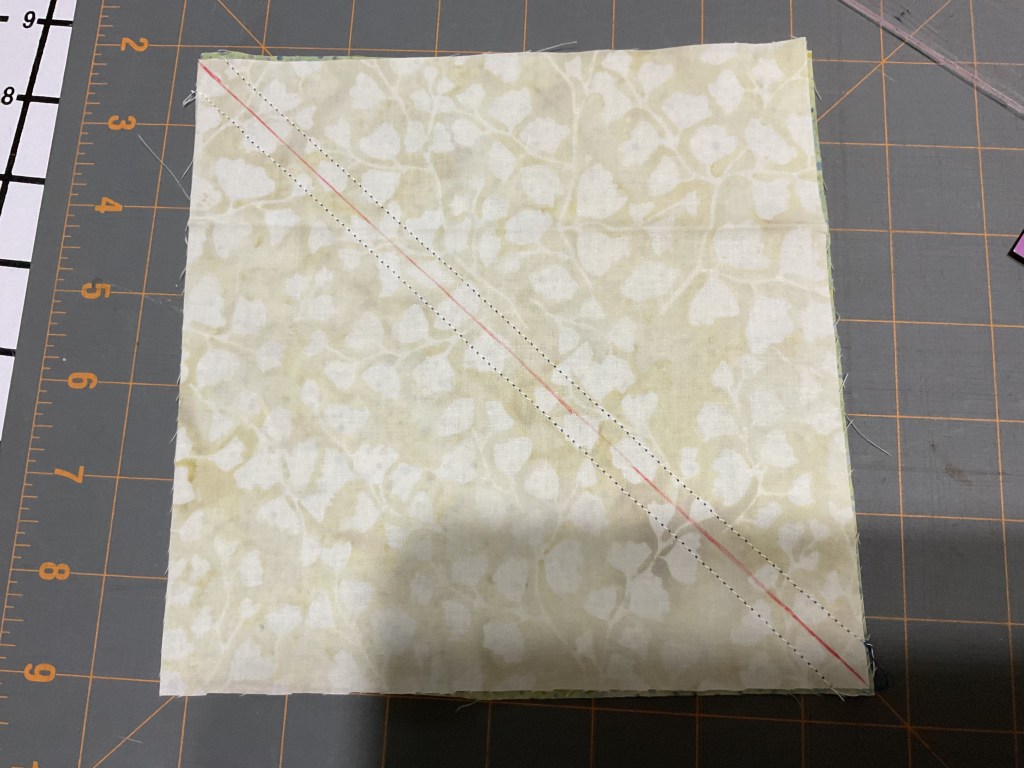 A fabric square with a diagonal marking for cutting, placed on a cutting mat.