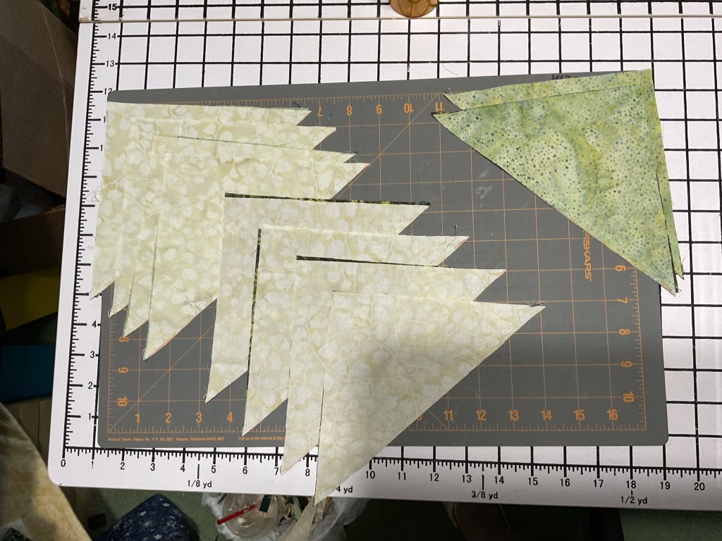 Cut fabric pieces for quilting, including triangles and patches, arranged on a cutting mat with grid lines.