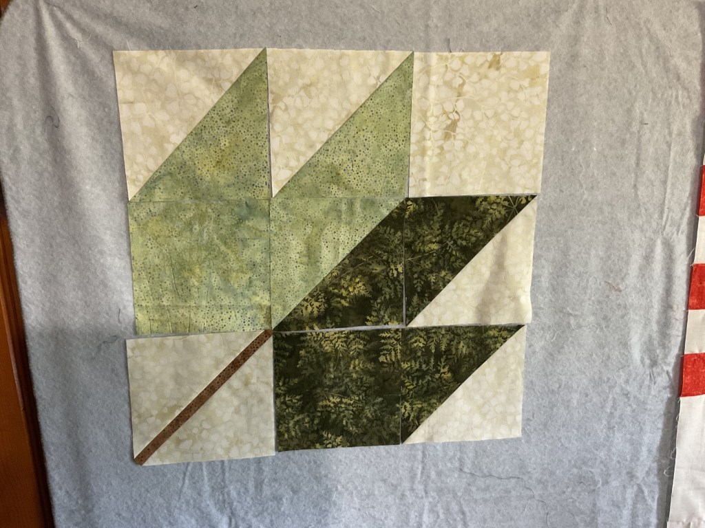 Close-up of a quilt block featuring a two-toned leaf design in green and beige fabric, displayed on a light gray fabric backdrop.