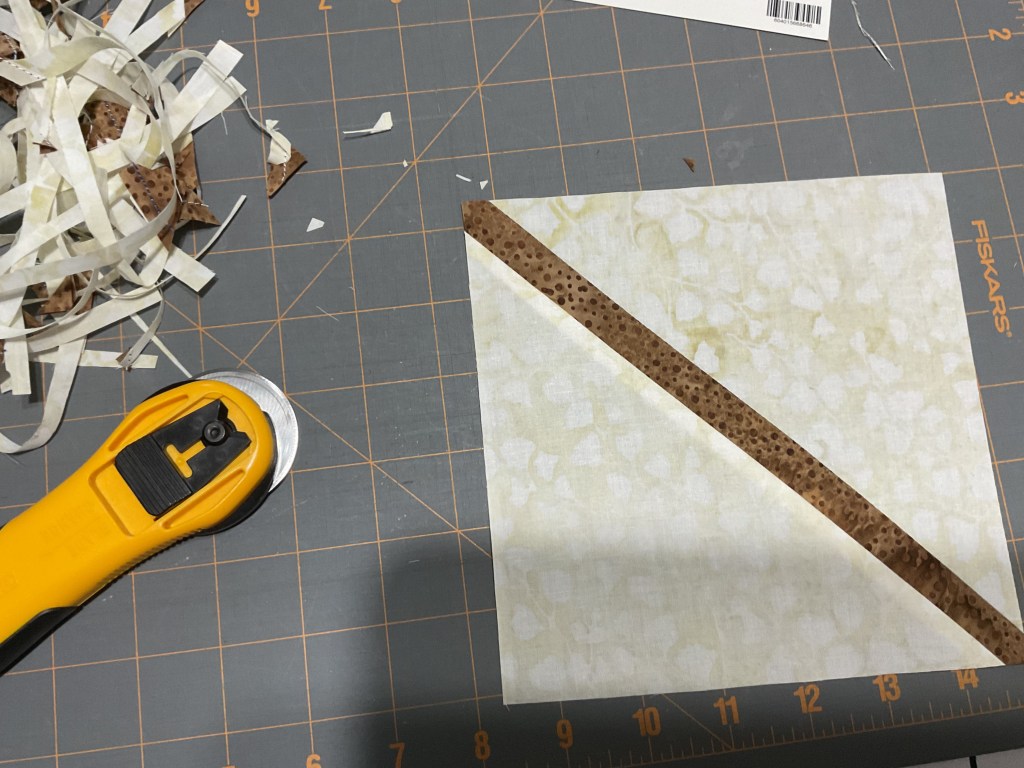 A rotary cutter and fabric pieces on a cutting mat, with decorative fabric scraps nearby.