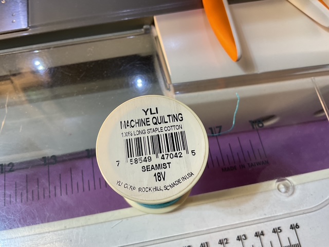 A spool of YLI machine quilting thread labeled 'Seamist', displaying the barcode and specifications on the side.