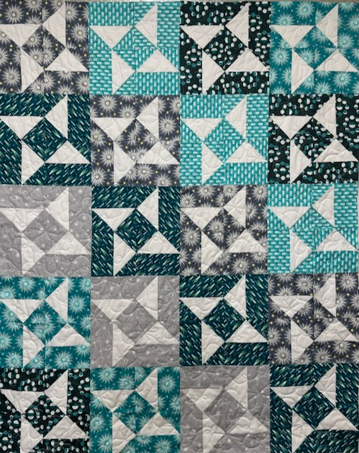 A colorful quilt featuring a geometric pattern with shades of teal, gray, and white, showcasing various block designs in a patchwork layout.
