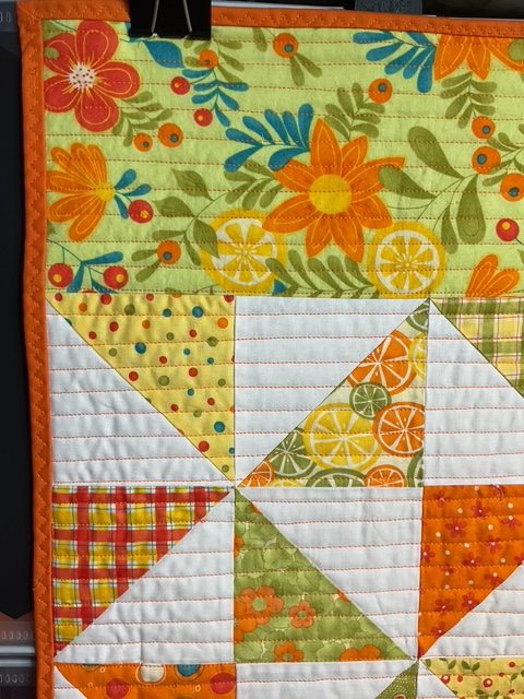 A close-up view of a quilted table runner featuring vibrant summer colors, floral patterns, and citrus motifs, showcasing intricate quilting lines.