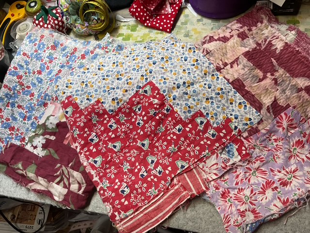 A collection of vintage fabric pieces in various patterns and colors, including florals and stripes, arranged on a textured surface.