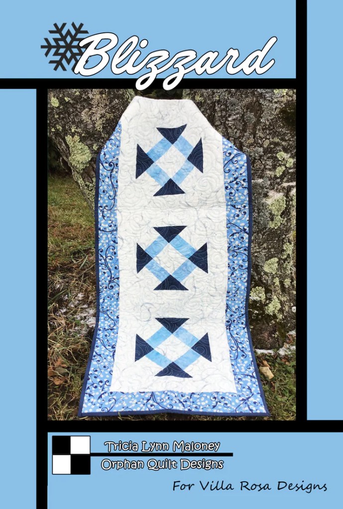 A quilt design titled 'Blizzard' featuring a blue color scheme with snowflake patterns, displayed against a natural background.