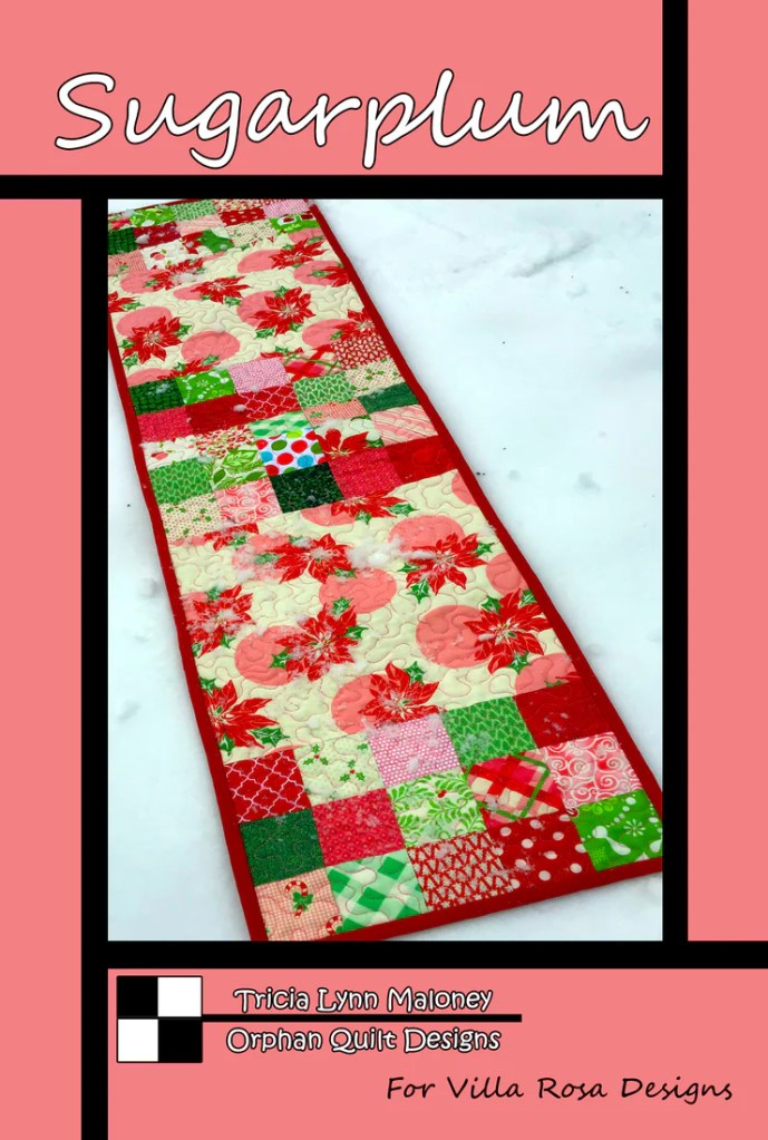 Colorful quilted table runner titled 'Sugarplum' with a patchwork design featuring red, green, and pink fabrics, set against a snowy background.