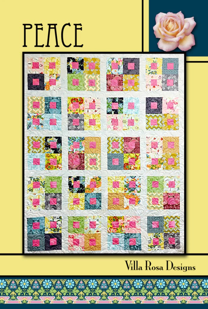 Colorful quilt titled 'Peace' featuring a patchwork design with various fabrics in shades of pink, green, blue, and yellow, displayed against a bright yellow background.