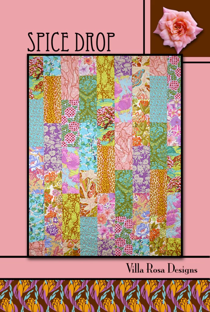 A colorful quilt pattern titled 'Spice Drop' featuring various vibrant fabrics in a patchwork design, surrounded by a pink background and floral border.