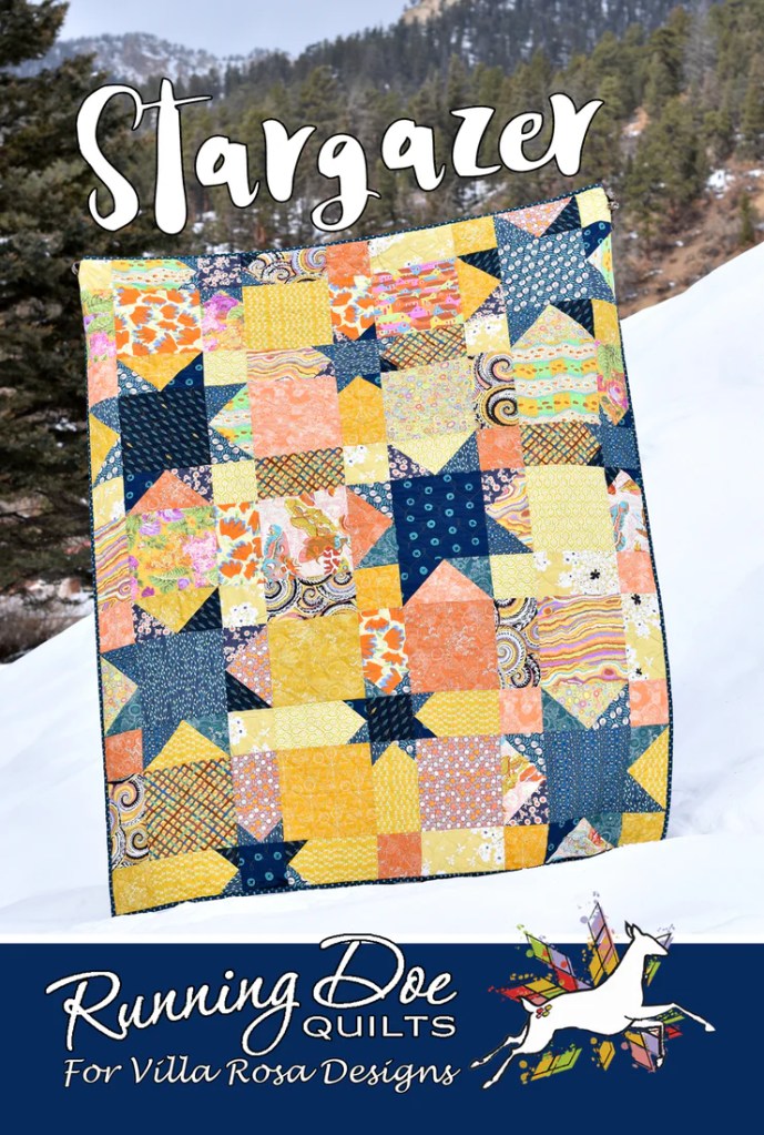 A colorful quilt titled 'Stargazer' displayed outdoors on snow, featuring various patterns in shades of yellow, blue, and orange, with text overlay by Running Doe Quilts for Villa Rosa Designs.