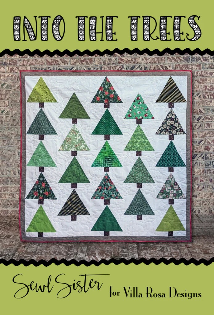 A quilt titled 'Into the Trees' featuring various green and patterned Christmas trees arranged in rows. The quilt is framed in red and is displayed against a textured wall.