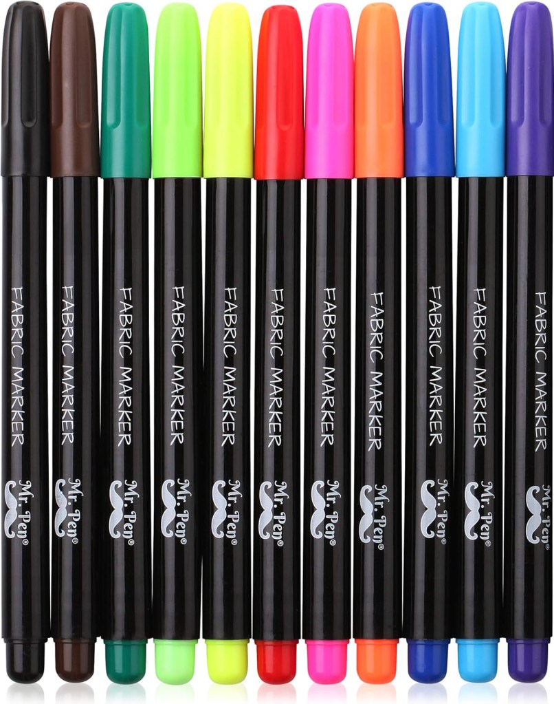 A set of colorful fabric markers arranged in a row, featuring various vibrant colors including brown, green, yellow, red, pink, and blue.