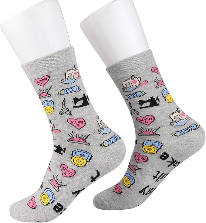 A pair of gray socks featuring various sewing-themed illustrations, including sewing machines, spools of thread, scissors, and pins.