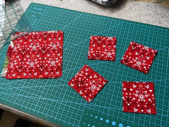 Red fabric pieces cut into small squares on a cutting mat with measurements.