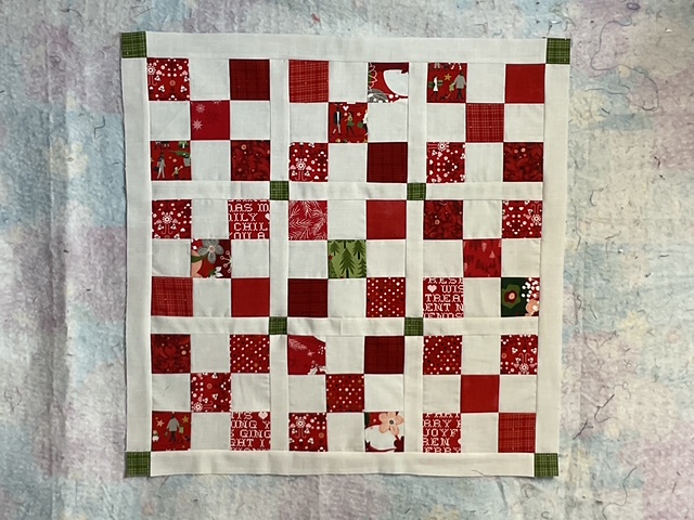 A patchwork quilt featuring red and white squares in a Nine Patch pattern, with seasonal holiday-themed fabrics.