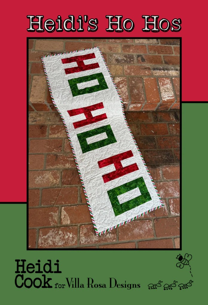 A holiday-themed table runner with 'HO HO HO' in red and green letters on a white quilted background, bordered with a candy cane-like striped pattern.