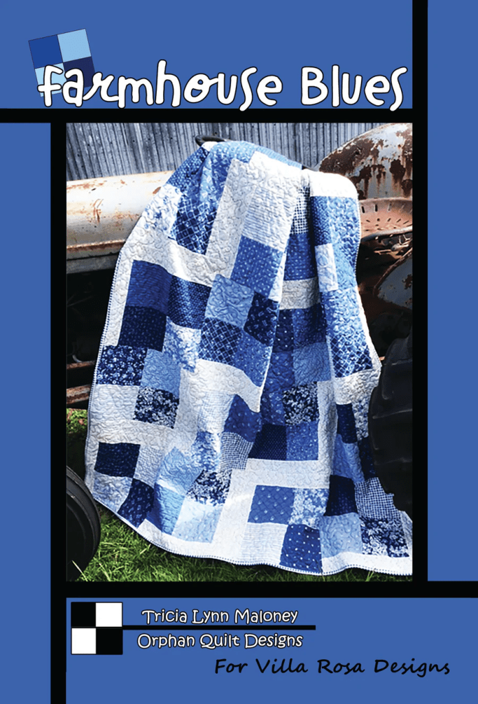 A quilt titled 'Farmhouse Blues' featuring a patchwork of various blue shades, draped over an old tractor, with textured patterns visible on the quilt fabric.