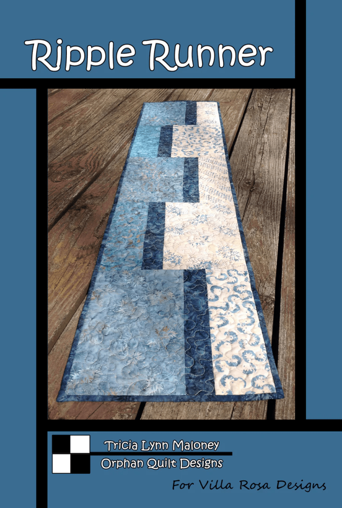 A quilted table runner displayed on a rustic wooden surface, featuring a ripple pattern in various shades of blue and white, with the title 'Ripple Runner' at the top.
