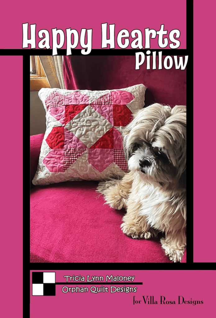 A decorative pillow with a heart design sits on a pink couch, accompanied by a small, fluffy dog.