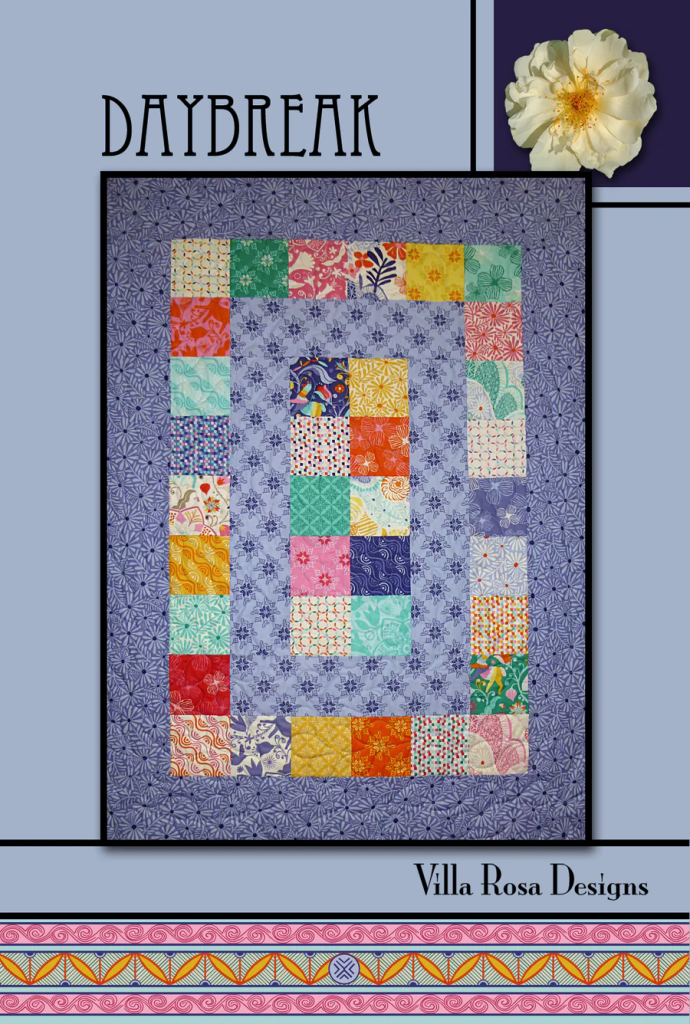 A colorful quilt titled 'Daybreak' designed by Villa Rosa Designs, featuring a patterned layout with various fabric squares, surrounded by a floral border.