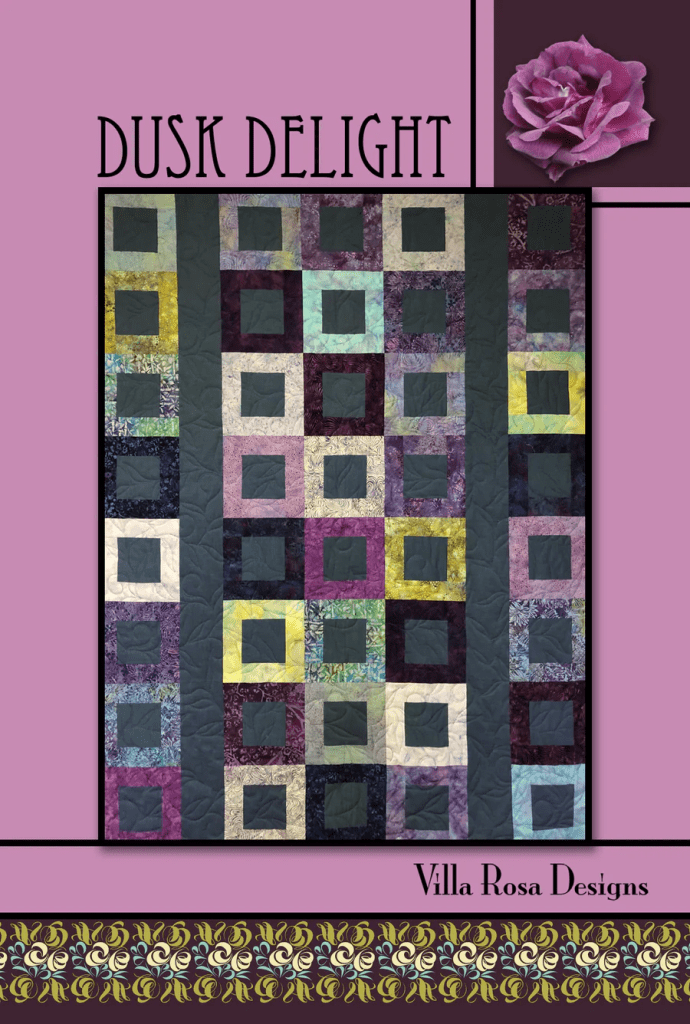 Colorful quilt design titled 'Dusk Delight' by Villa Rosa Designs, featuring a pattern of squares and rectangles in various shades of purple, blue, green, and black against a pink background, with a decorative floral border.