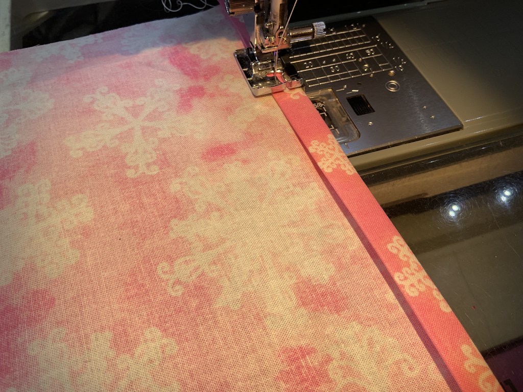 Close-up of a sewing machine stitching a decorative pink fabric with snowflake patterns.