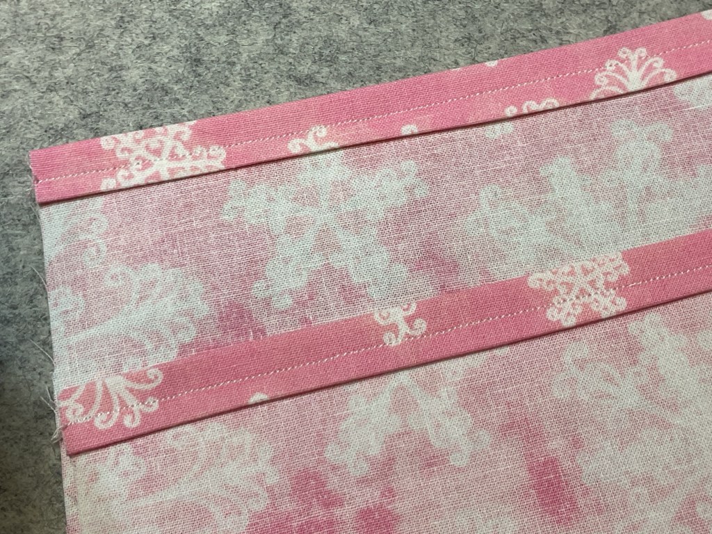 Close-up of a pink patterned fabric featuring white snowflake designs with visible stitching along the edges.