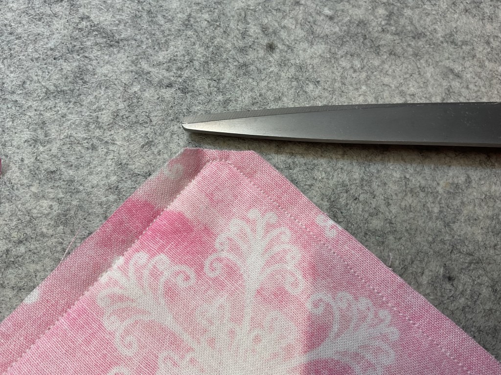 Close-up of pink patterned fabric with scissors cutting the edge on a gray felt background.